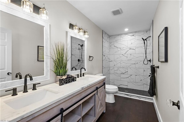 bathroom with wood-type flooring, a tile shower, vanity, and toilet