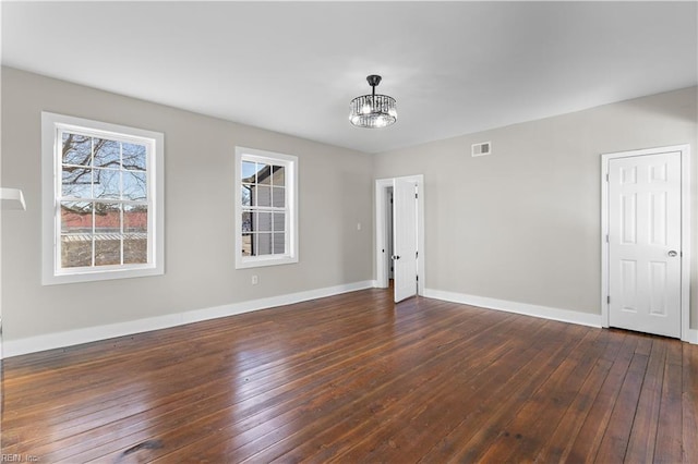 empty room with a notable chandelier and dark hardwood / wood-style flooring