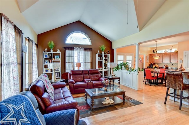 living room with a healthy amount of sunlight, high vaulted ceiling, light hardwood / wood-style flooring, and decorative columns