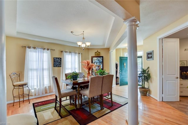 dining space with a notable chandelier, a raised ceiling, decorative columns, and hardwood / wood-style flooring