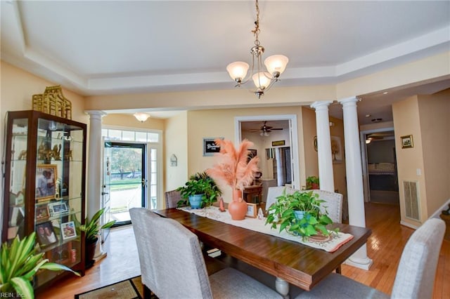 dining room featuring ceiling fan with notable chandelier, a raised ceiling, and light hardwood / wood-style flooring