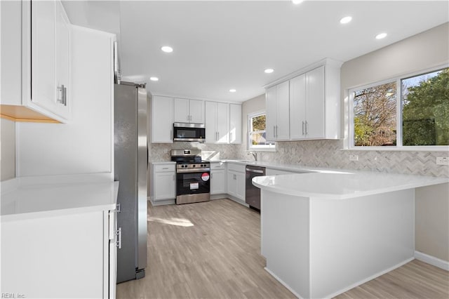 kitchen with kitchen peninsula, appliances with stainless steel finishes, light hardwood / wood-style flooring, and white cabinets