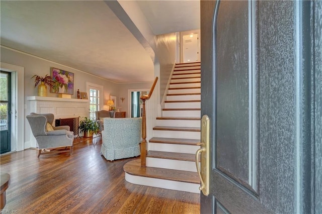 stairs featuring a brick fireplace, crown molding, and wood-type flooring