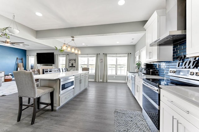 kitchen with wall chimney exhaust hood, white cabinetry, stainless steel appliances, backsplash, and a breakfast bar area