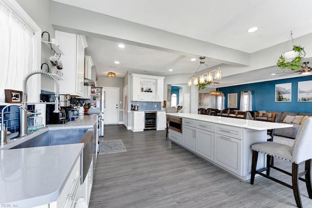 kitchen with wine cooler, a kitchen island, decorative backsplash, hanging light fixtures, and white cabinets