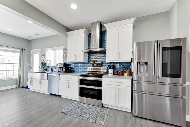 kitchen featuring appliances with stainless steel finishes, white cabinetry, wall chimney range hood, tasteful backsplash, and sink