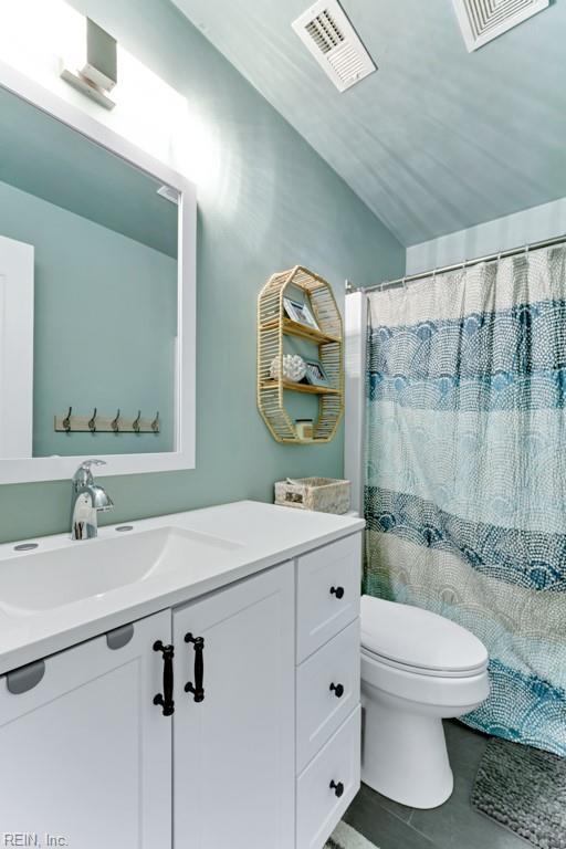 bathroom featuring curtained shower, lofted ceiling, tile patterned flooring, vanity, and toilet