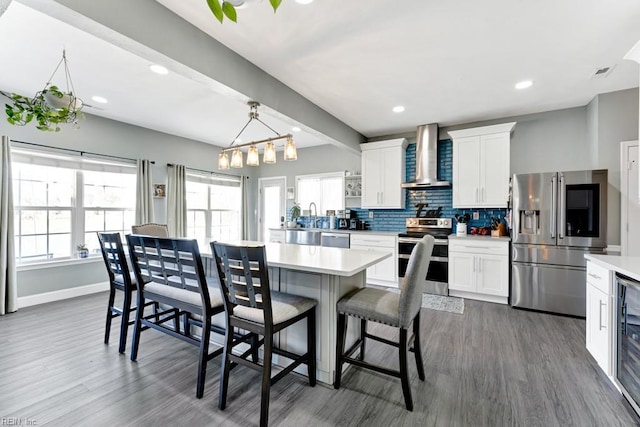 kitchen featuring appliances with stainless steel finishes, wall chimney exhaust hood, beam ceiling, and white cabinets