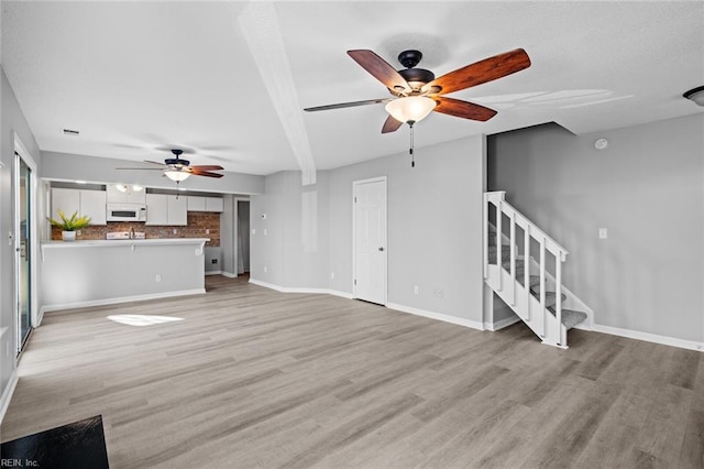 unfurnished living room with beam ceiling, ceiling fan, and light hardwood / wood-style flooring