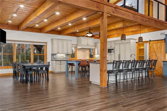 dining room featuring wood ceiling, beamed ceiling, dark hardwood / wood-style floors, ceiling fan, and a barn door