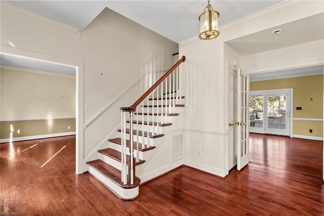 staircase with wood-type flooring, ornamental molding, and a chandelier