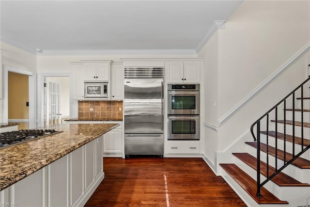 kitchen with built in appliances, crown molding, light stone counters, white cabinetry, and tasteful backsplash