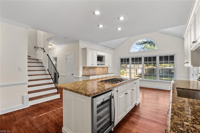 kitchen with beverage cooler, dark stone countertops, stainless steel gas cooktop, white cabinets, and sink