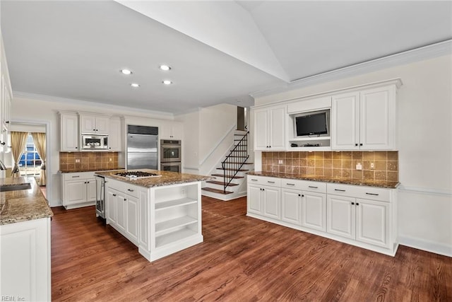 kitchen with built in appliances, white cabinets, vaulted ceiling, an island with sink, and dark stone counters