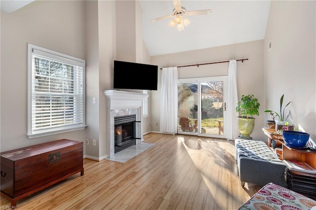 living room with high vaulted ceiling, a premium fireplace, ceiling fan, and light wood-type flooring