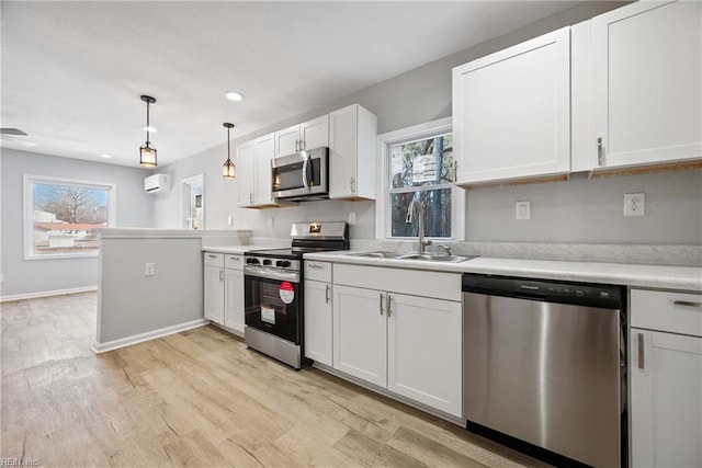 kitchen featuring white cabinetry, stainless steel appliances, decorative light fixtures, an AC wall unit, and sink