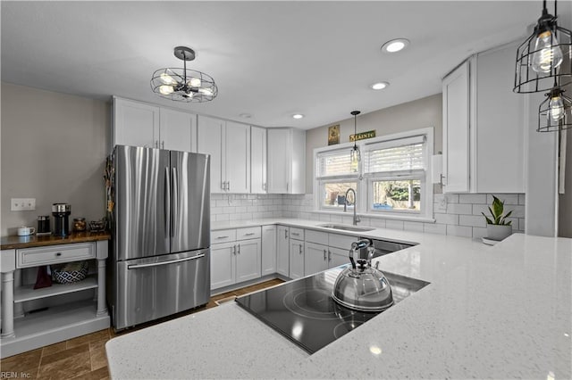 kitchen featuring sink, white cabinetry, stainless steel refrigerator, and light stone countertops