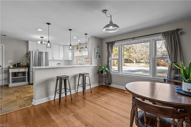 kitchen featuring stainless steel refrigerator, hanging light fixtures, kitchen peninsula, white cabinets, and tasteful backsplash