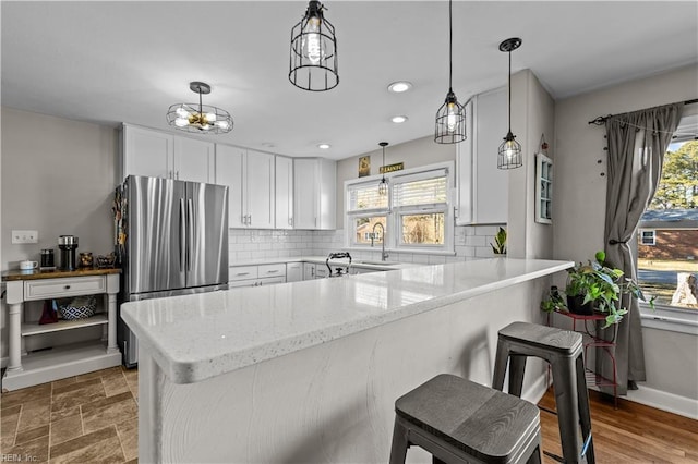 kitchen featuring kitchen peninsula, stainless steel fridge, white cabinets, and a breakfast bar area