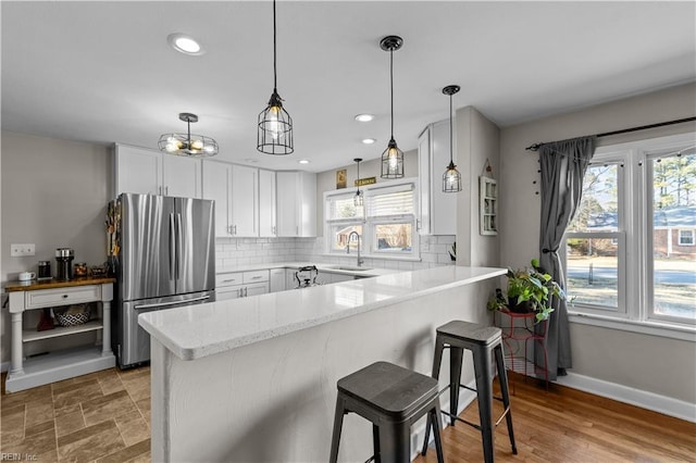 kitchen featuring kitchen peninsula, a wealth of natural light, a breakfast bar area, stainless steel refrigerator, and white cabinets