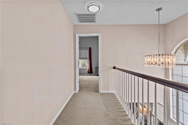 hall with light colored carpet and a notable chandelier