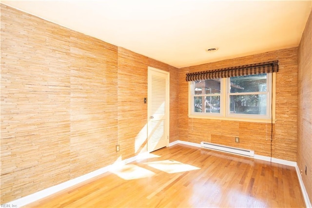 empty room with hardwood / wood-style flooring, wood walls, and a baseboard radiator