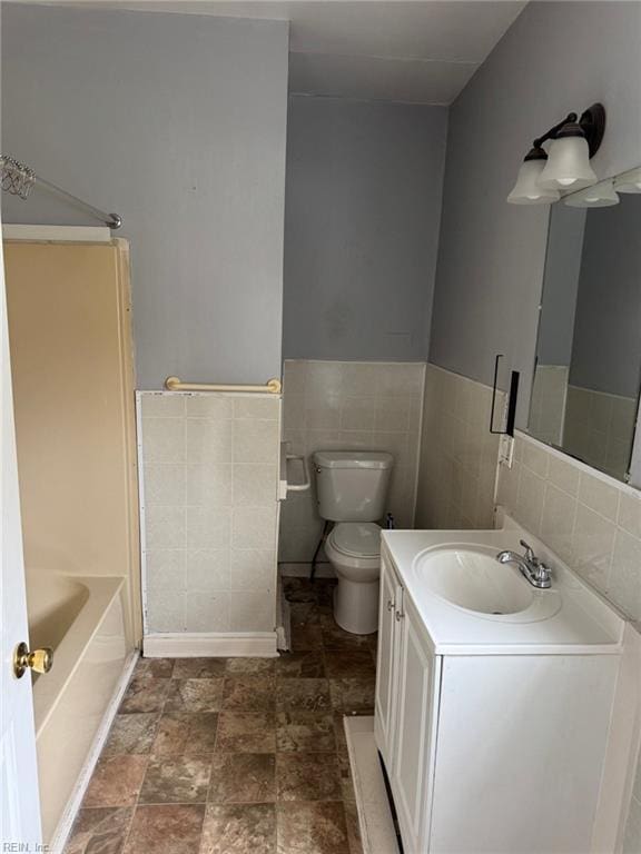 bathroom featuring toilet, a tub, tile walls, and vanity