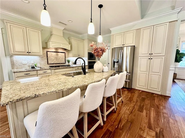 kitchen with custom exhaust hood, appliances with stainless steel finishes, decorative backsplash, sink, and cream cabinets