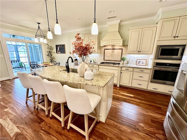 kitchen with decorative light fixtures, stainless steel appliances, premium range hood, and cream cabinets