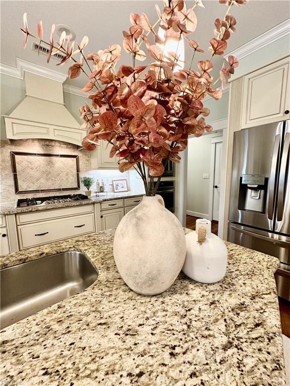 kitchen featuring light stone counters, stainless steel appliances, cream cabinets, and crown molding