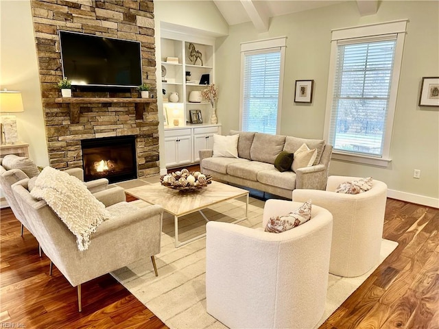 living room with light hardwood / wood-style floors, a stone fireplace, vaulted ceiling with beams, and built in shelves