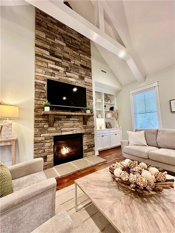 living room featuring a fireplace, built in features, light hardwood / wood-style flooring, and vaulted ceiling with beams