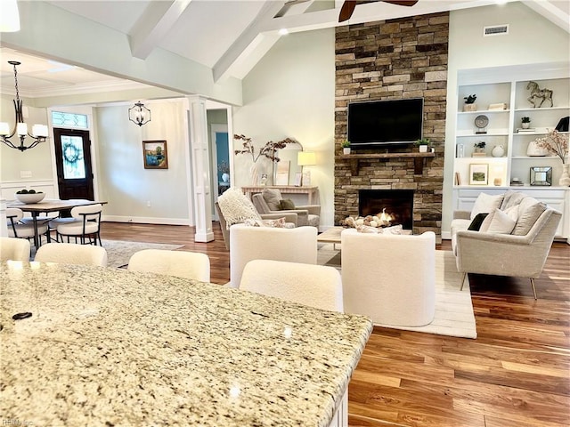 living room with hardwood / wood-style floors, ceiling fan with notable chandelier, lofted ceiling with beams, and a stone fireplace