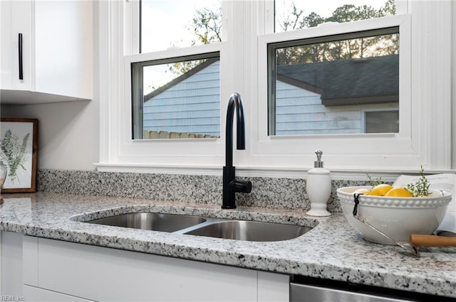 room details featuring light stone counters, white cabinets, stainless steel dishwasher, and sink