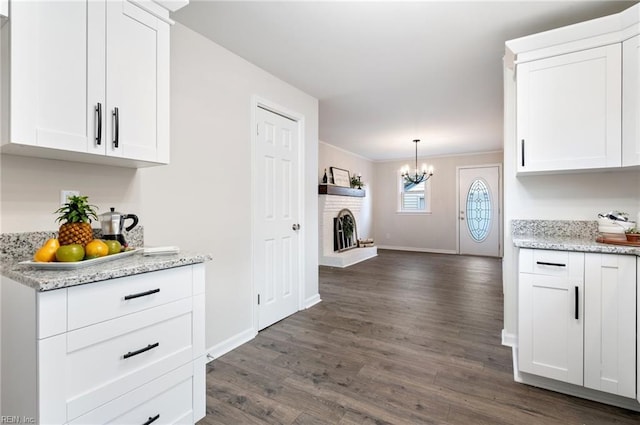 kitchen with light stone countertops, a chandelier, dark hardwood / wood-style floors, hanging light fixtures, and white cabinetry