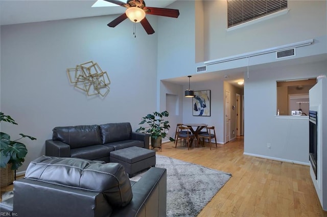 living room with ceiling fan, a skylight, light hardwood / wood-style floors, and high vaulted ceiling