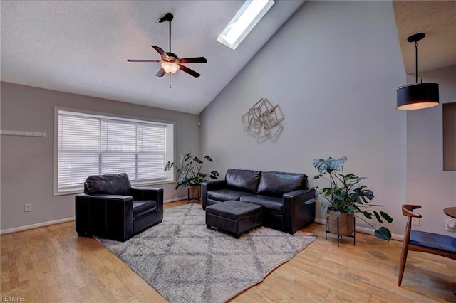 living room with ceiling fan, vaulted ceiling with skylight, and wood-type flooring