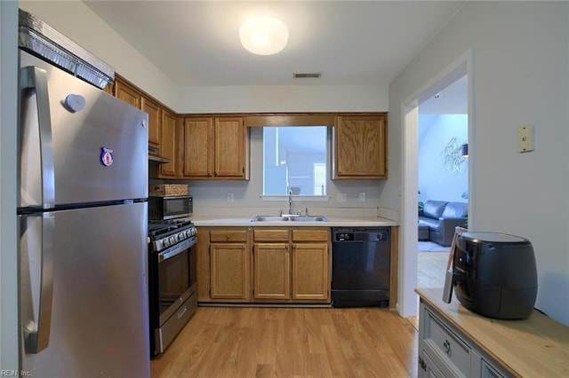 kitchen with exhaust hood, stainless steel appliances, light hardwood / wood-style floors, and sink