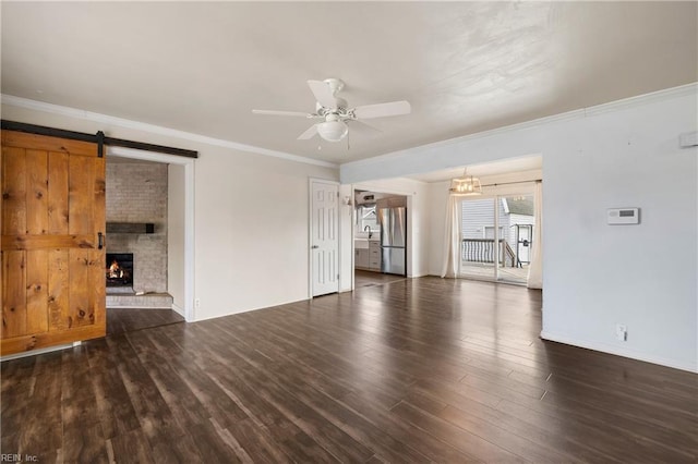 unfurnished living room with ceiling fan, a fireplace, dark hardwood / wood-style floors, and a barn door