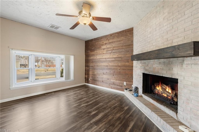 unfurnished living room featuring a textured ceiling, dark hardwood / wood-style flooring, a fireplace, wood walls, and ceiling fan