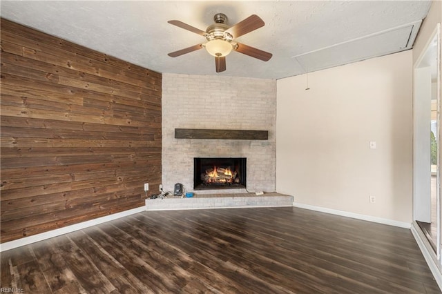 unfurnished living room featuring a textured ceiling, dark wood-type flooring, a brick fireplace, wood walls, and ceiling fan