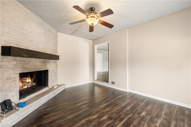 unfurnished living room featuring ceiling fan, a fireplace, a textured ceiling, and dark wood-type flooring