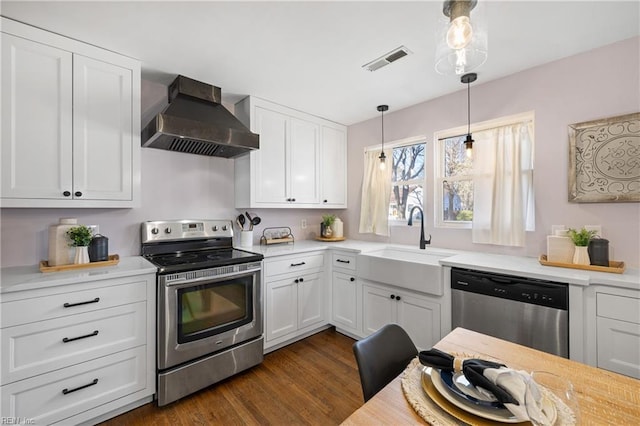 kitchen featuring white cabinetry, appliances with stainless steel finishes, decorative light fixtures, wall chimney exhaust hood, and sink