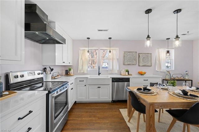 kitchen featuring wall chimney range hood, pendant lighting, sink, stainless steel appliances, and white cabinets