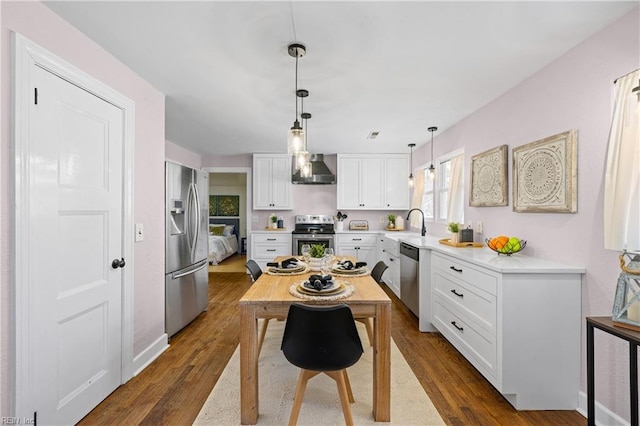 kitchen with stainless steel appliances, dark hardwood / wood-style flooring, wall chimney range hood, pendant lighting, and white cabinets