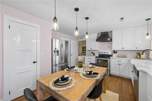 kitchen with white cabinetry, appliances with stainless steel finishes, hanging light fixtures, wall chimney range hood, and sink