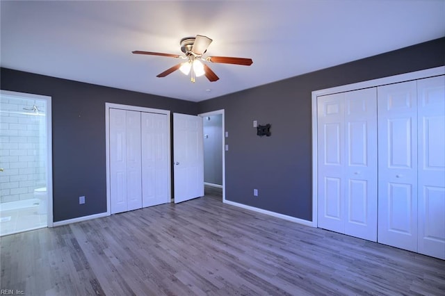 unfurnished bedroom with two closets, ceiling fan, wood-type flooring, and connected bathroom