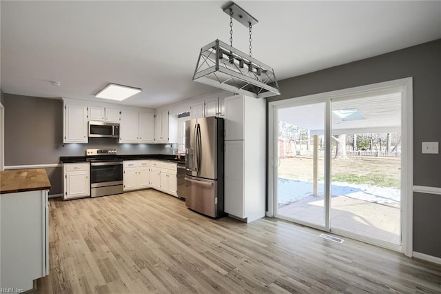 kitchen with white cabinets, light wood-type flooring, hanging light fixtures, and appliances with stainless steel finishes