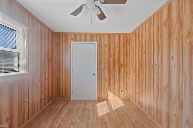 spare room with ceiling fan, light hardwood / wood-style flooring, and wooden walls