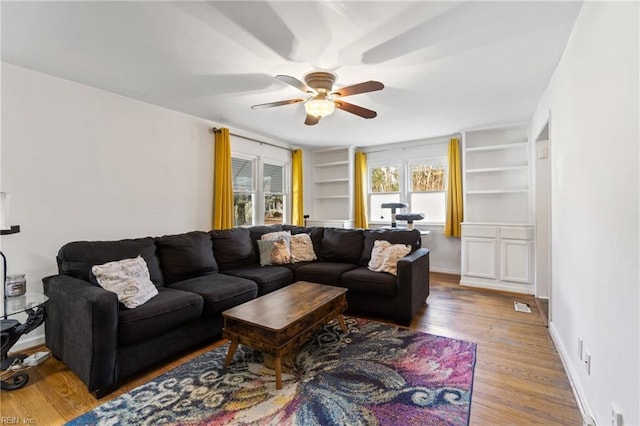 living room with built in features, ceiling fan, and hardwood / wood-style floors